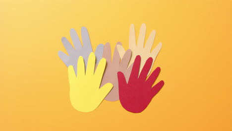 Close up of hands together made of colourful paper on orange background with copy space