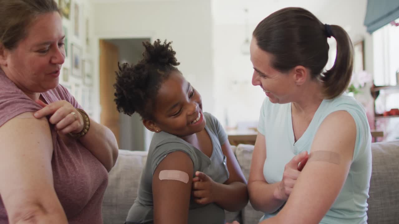 Caucasian lesbian couple and their african american daughter pointing at bandages on their arms