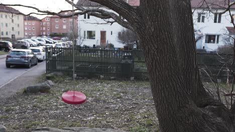 a lonely red swing moving around from the wind and hanging in a tree