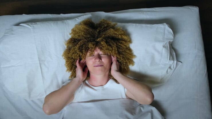 Woman wearing wireless headphones enjoy listening to music with closed eyes while lying in bed at night before going to sleep