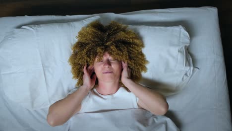 woman wearing wireless headphones enjoy listening to music with closed eyes while lying in bed at night before going to sleep