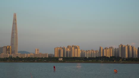 Torre-De-Lotería-Y-Gente-Haciendo-Windsurf-Y-Surf-Con-Ala-De-Eco-Al-Atardecer,-Fondo-Urbano-Del-Apartamento-Jamsil,-Horizonte-De-La-Ciudad-De-Seúl