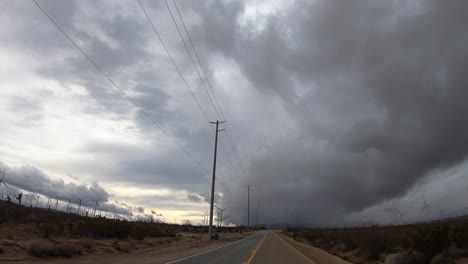 driving hyperlapse by windmills with storm clouds on rural road in mojave desert