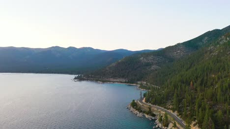 aerial drone view of cars driving on lakeside road with mountains and blue water of lake tahoe in the sierra nevada on cloudy day