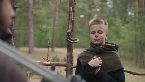 teenage boy with sword looks at knight in military camp