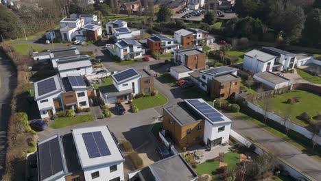 aerial orbital view of upscale sustainable housing development with angular timber and white facades, rooftop solar panels, geometric landscaping and open green space nearby