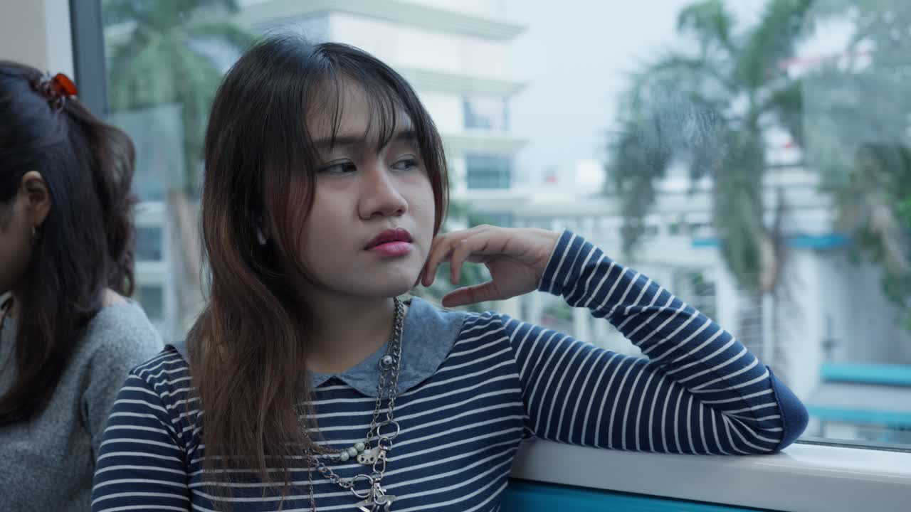 Young woman in striped shirt blinking slowly while sitting on a train, eyes closed briefly
