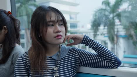 young woman in striped shirt blinking slowly while sitting on a train, eyes closed briefly