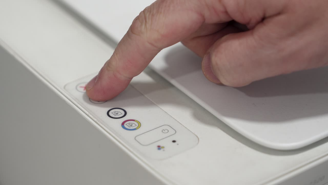 A person is using their finger to press a button on a printer. The printer is located on an office desk. The action is intended to start a print job for documents