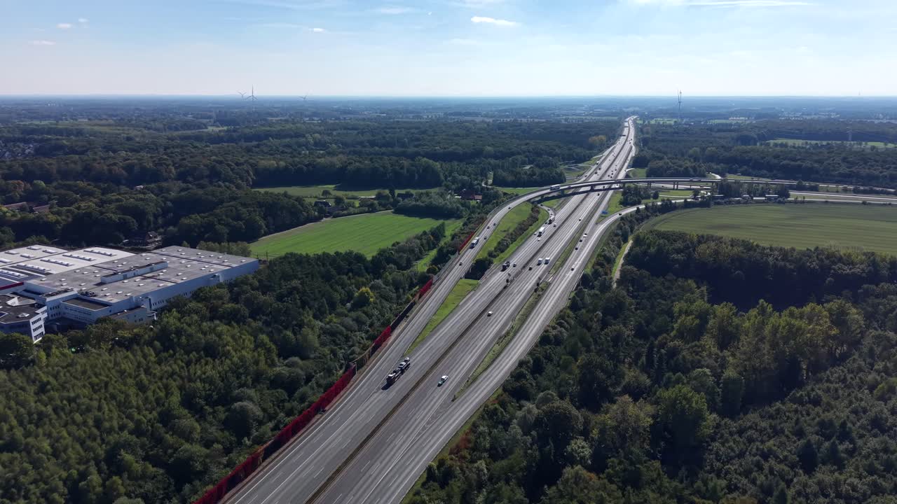 Traffic scene on Multi-lane highway in america surrounded by green forest landscape and warehouses in suburb. Aerial forward wide shot. Sunny morning with many cars