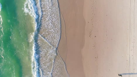 A-couple-walking-along-Tennyson-Beach-in-Adelaide,-South-Australia-as-waves-gently-roll-into-shore