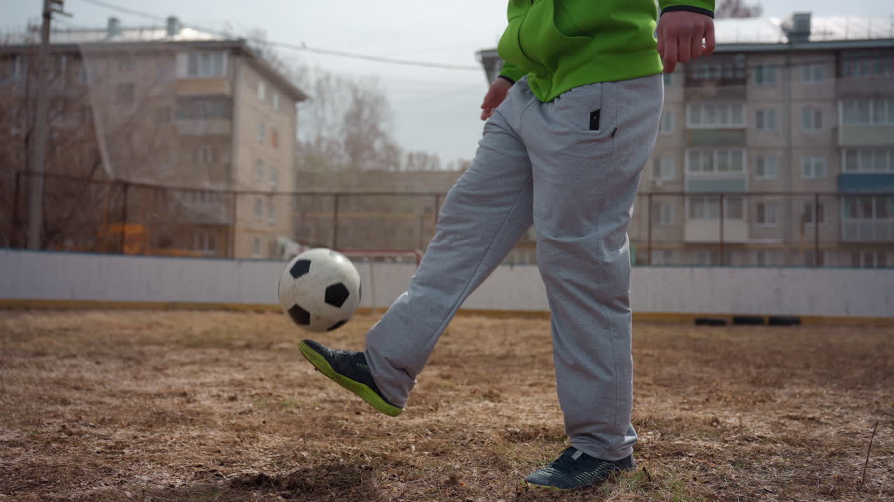 Persona habilidosa haciendo malabares con una pelota en un patio, entrenamiento informal con movimiento constante y toques suaves; atleta concentrado realizando ejercicios rutinarios en el campo del patio de un apartamento de la ciudad