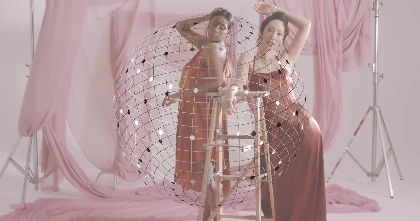Con una sfera 3D fluttuante al centro di un servizio fotografico di moda rosa, due modelle posano intorno a una scaletta.