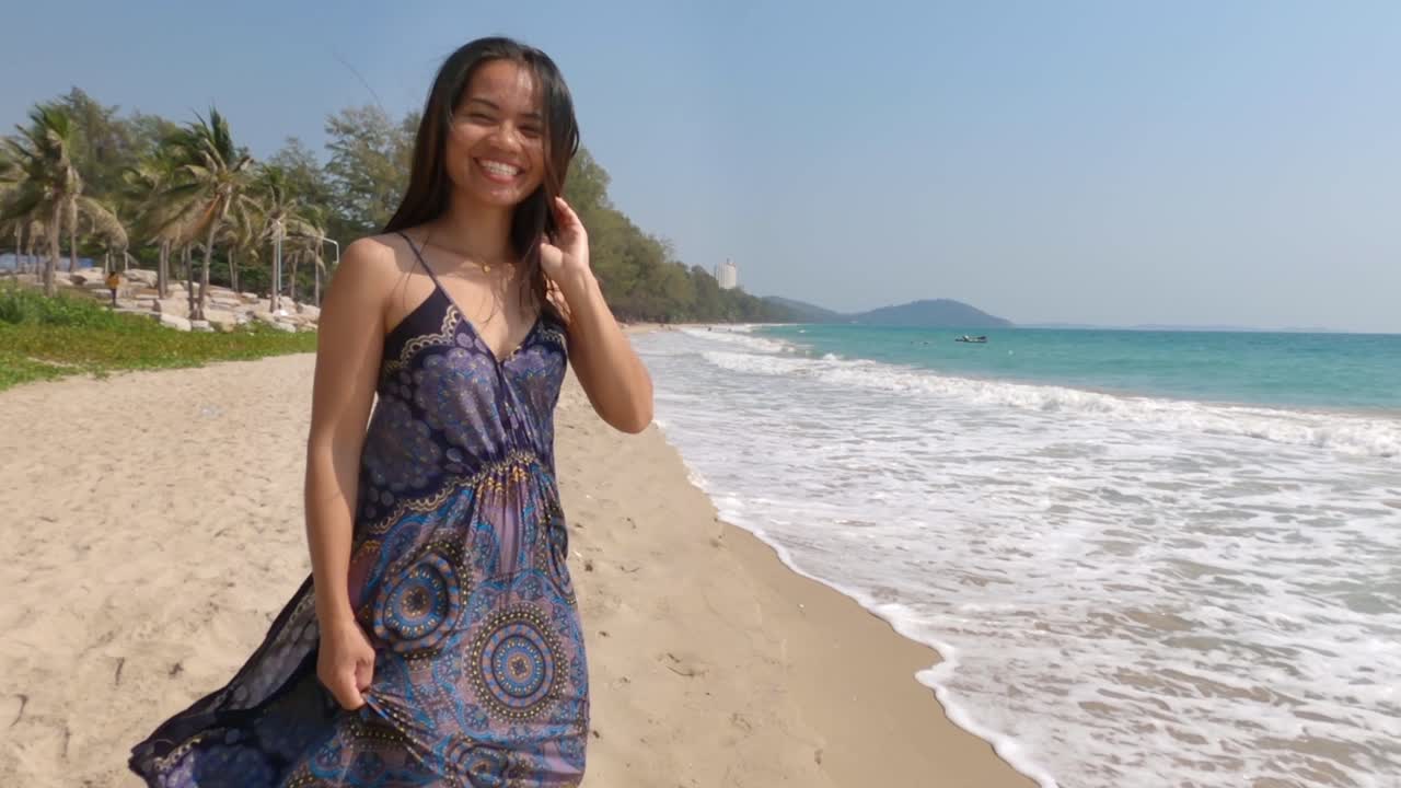 bella dama tailandesa caminando alegremente en la arena de la playa en tailandia con olas salpicando en la orilla en un día de verano - tiro medio