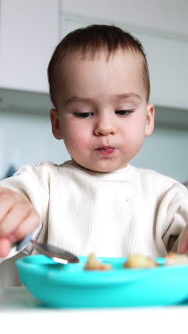 little kid eating from plate using spoon. baby is growing , developing and learning. vertical video