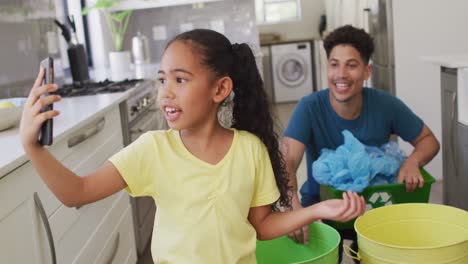 Feliz-Padre-E-Hija-Birraciales-Haciendo-Videollamadas-Usando-Un-Teléfono-Inteligente,-Clasificando-Residuos-Juntos