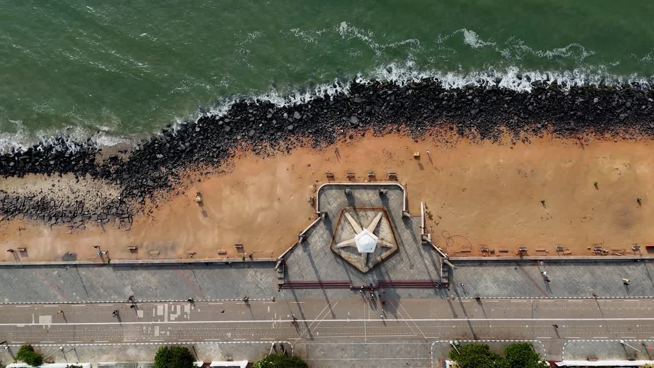 Early morning aerial footage looks inland from the Bay of Bengal. The video showcases the iconic Mahatma Gandhi statue symbolizing the city's unique charm as it meets the sea. People walking on road