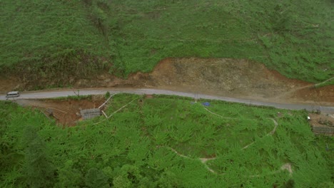 Aerial-view-of-a-mountain-road-in-Sapa,-Vietnam,-surrounded-by-lush-green-hills-and-farmland