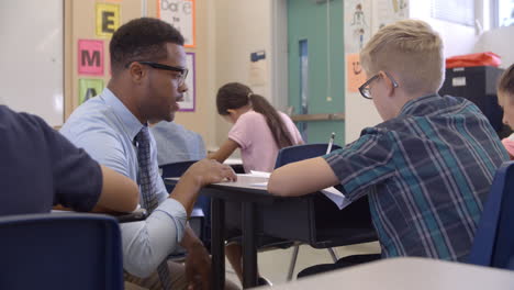 teacher kneeling to help a 5th grade schoolboy at his desk