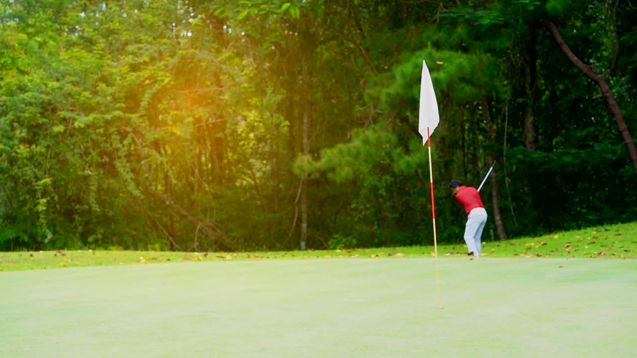 Golf sport concept, Golfer hitting golf ball on bunker of golf course in beautiful fairway and layout. Red flag on green and wind blowing.