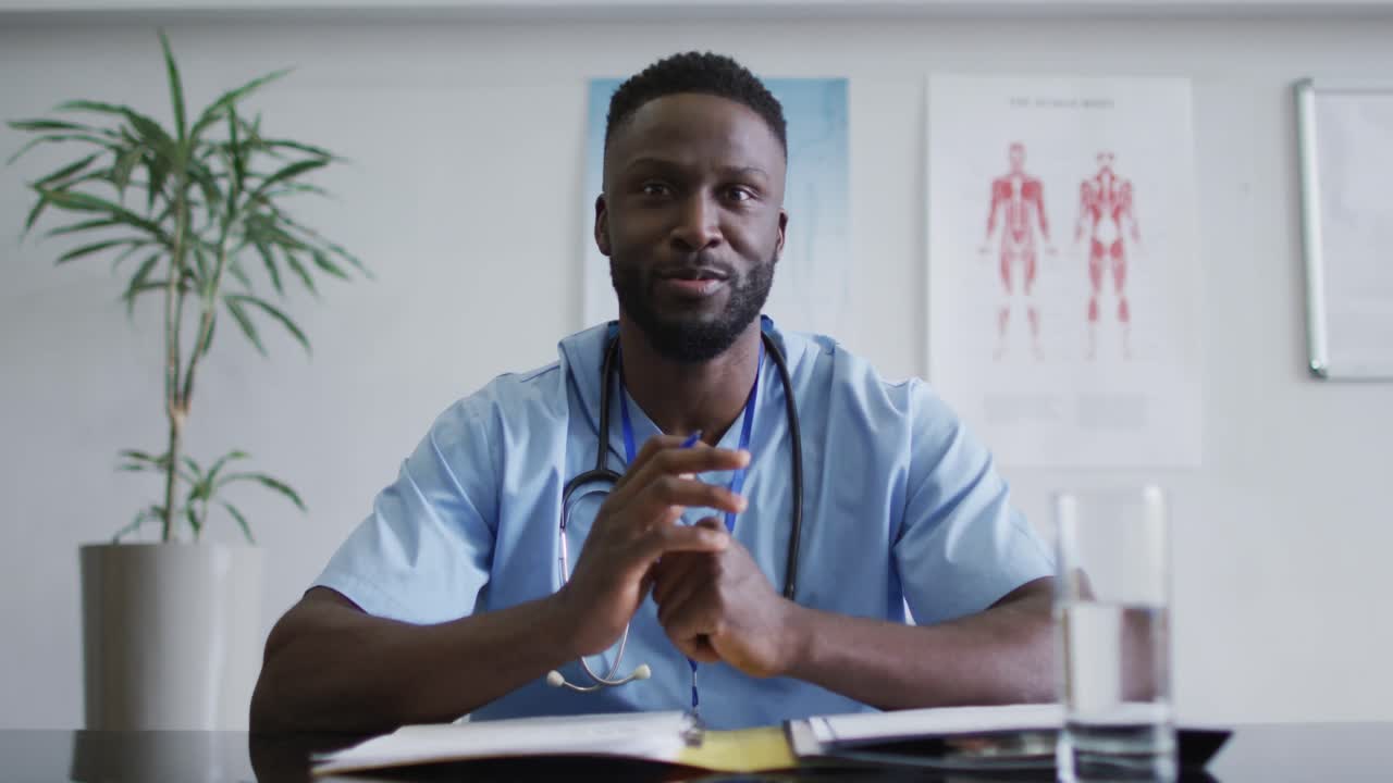 médico afroamericano de sexo masculino en el escritorio hablando y gestando durante la consulta de videollamada