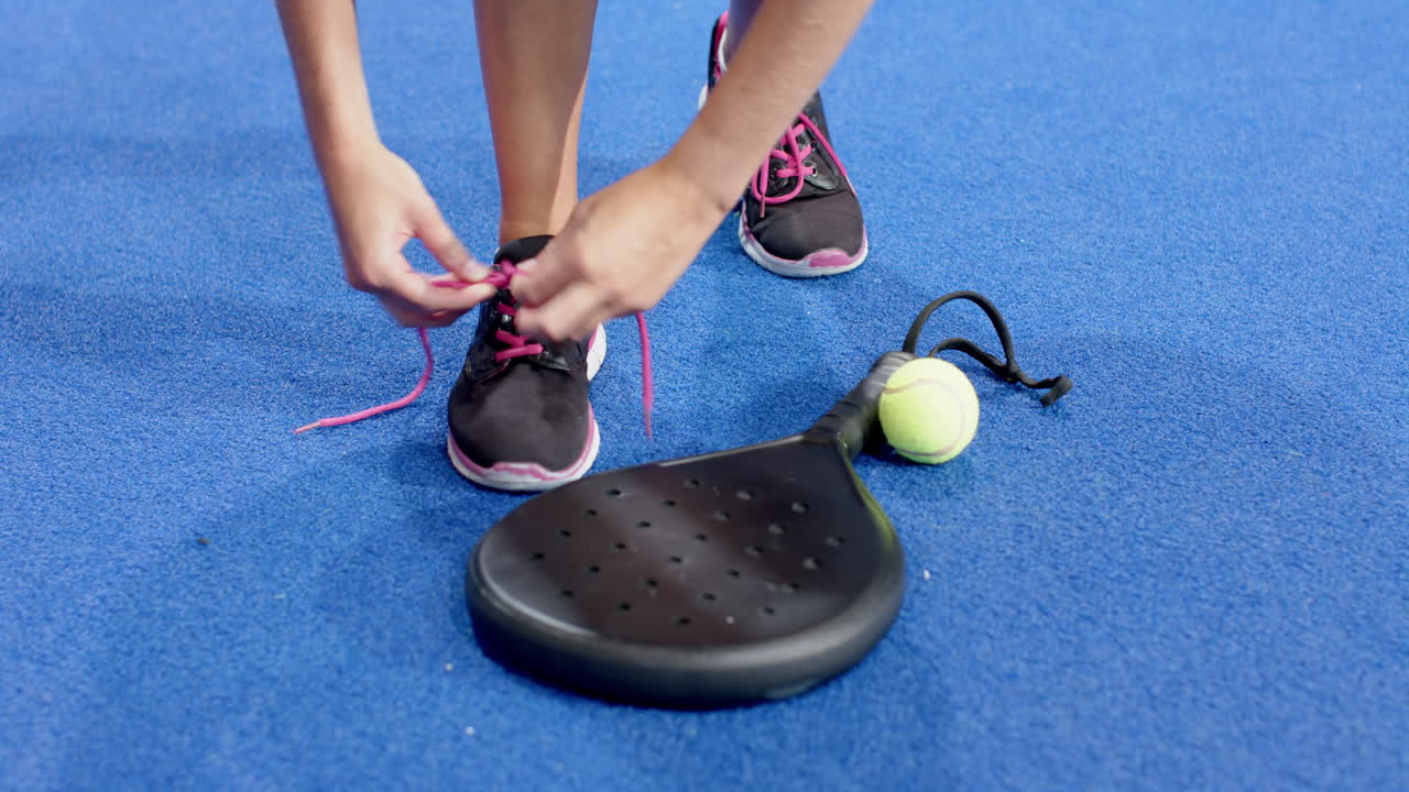 Tying shoelaces, person preparing for padel tennis match with racket and ball, at indoor court