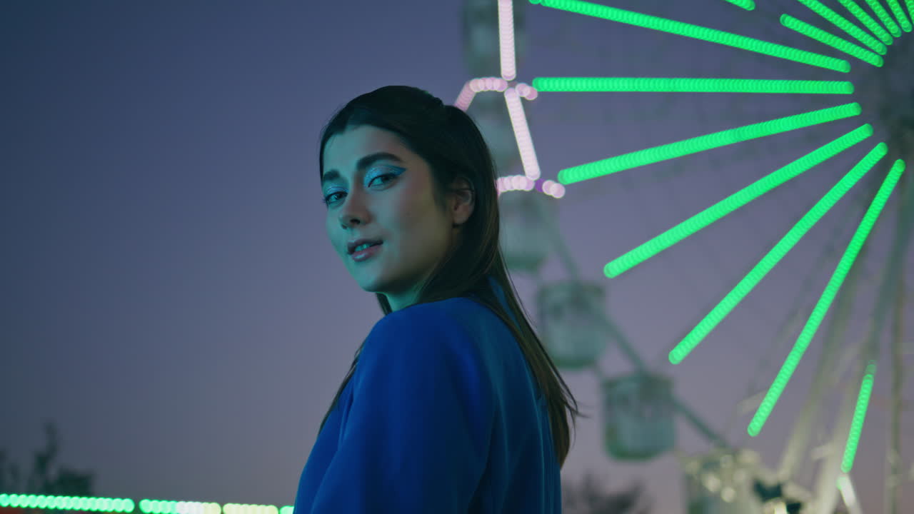 아름다운 모델이 조명된 놀이 공원에서 페리스 을 포즈하고 있습니다.