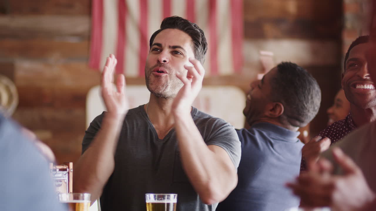 grupo de amigos masculinos celebrando mientras ven el juego en la pantalla en un bar deportivo