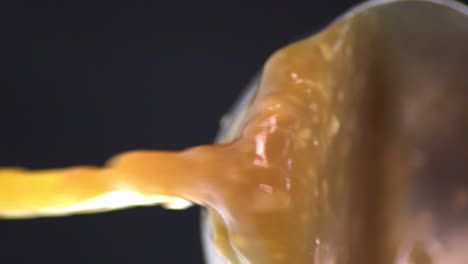 vista en perspectiva horizontal volteada de una mezcla de alimentos coagulados gruesos líquidos amarillos aislados para cocinar pollo mentai que se vierte del tazón de plata, fondo negro, estática de primer plano extremo