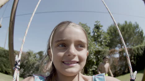 closeup of cute girl riding on swings in backyard on sunny day.