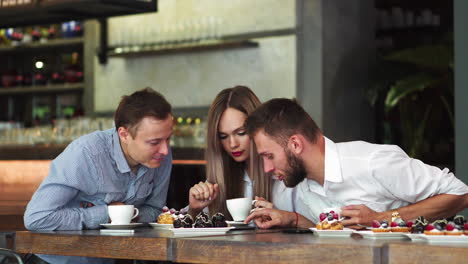 three students sitting together at their working place, writing with pencils and studying scientific literature, preparing for exams in university. bearded guy and two females working on project