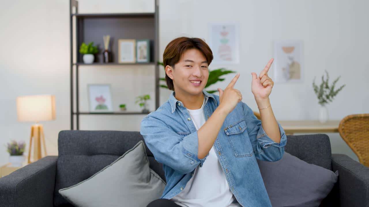소파에 앉아 미소를 지으며 카피 스페이스를 가리키는 행복한 젊은 성인 남성