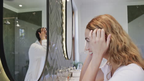 happy caucasian lesbian couple looking in mirror, touching face and smiling in bathroom