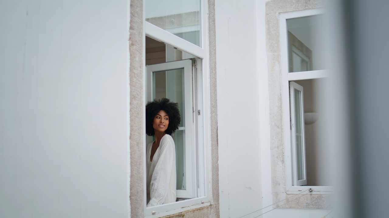 Tender model leaning window frame white house. Curly woman posing camera alone