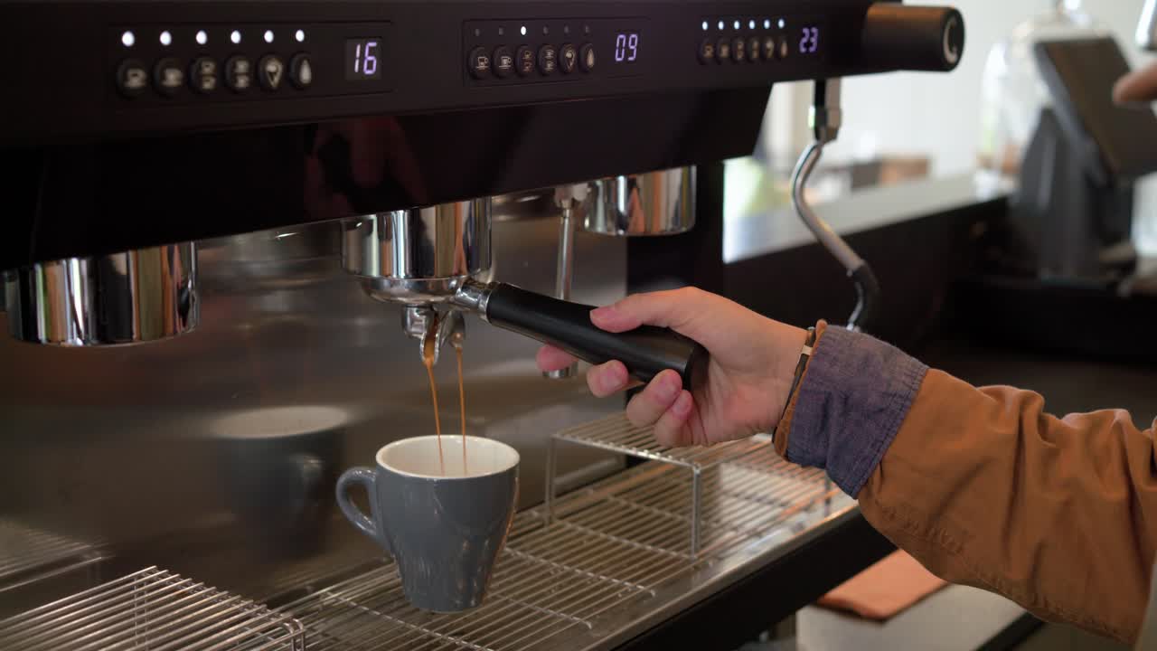 Il barista blocca il portafiltro sotto il gruppo erogatore e preme il pulsante di erogazione, estraendo l'espresso in una tazza.