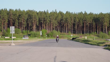 мотоциклист в шлеме на дороге в лесу приближается к камере