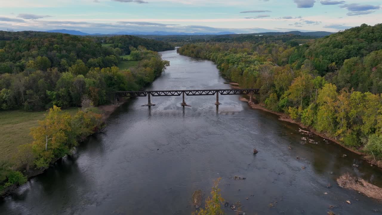 Aerial birds eye shot of tranquil river with old bridge surrounded by colorful trees. Early morning in forest landscape of America. Wide shot.