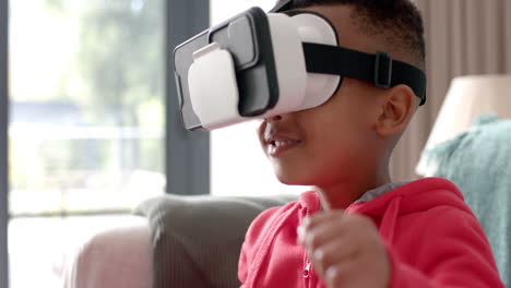 African-american-boy-using-vr-headset-and-touching-virtual-screen-in-living-room,-slow-motion