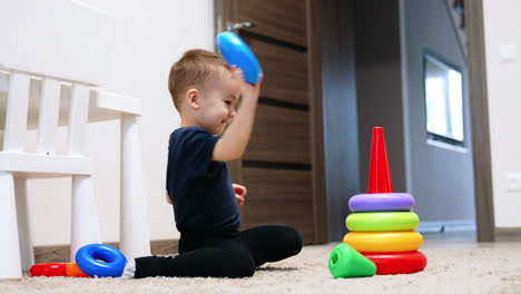 cute smiling caucasian toddler sits on the floor. baby boy assembling the pyramid in his room.