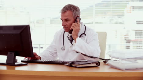 Doctor picking up the phone and using his computer