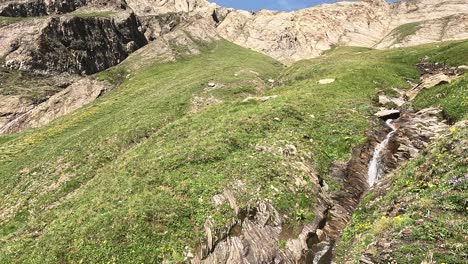 vista sobre una cascada que baja por las empinadas laderas cubiertas de hierba de las llanuras italianas en el alpe bettelmann