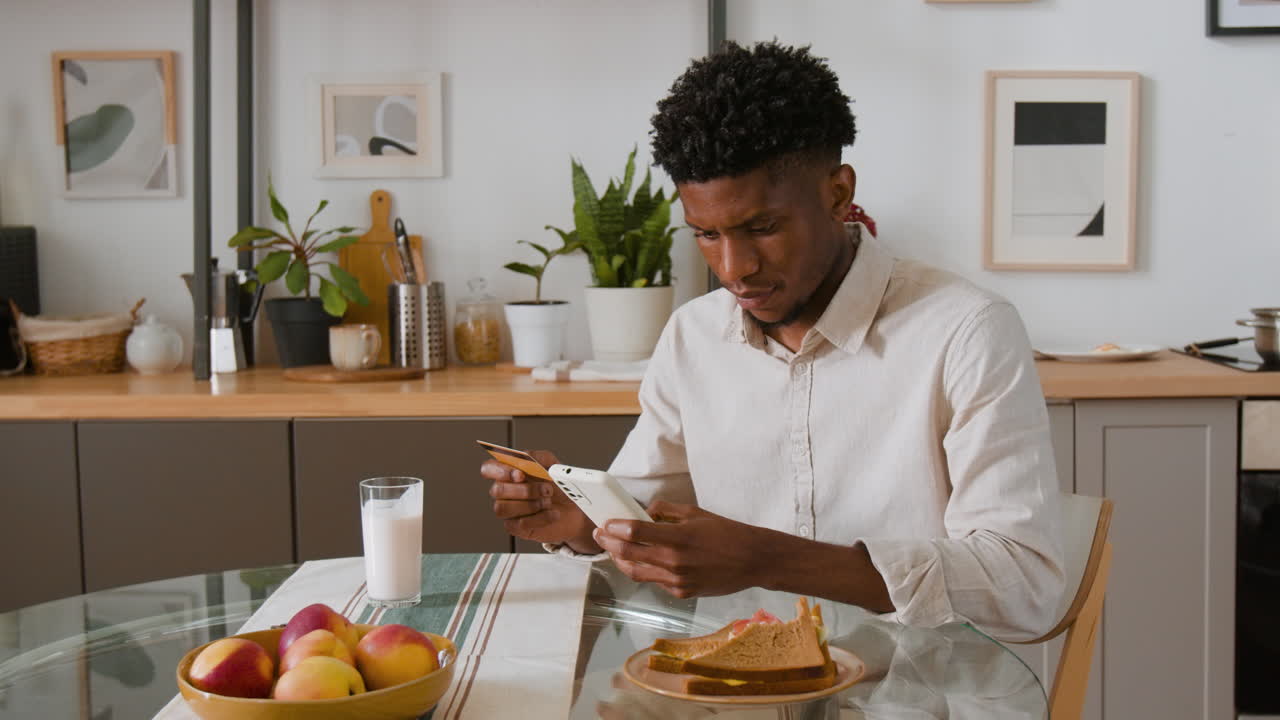 Man using smartphone with credit card in the kitchen