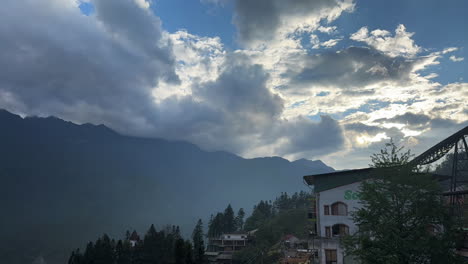 clouds moving fast over misty mountains and town buildings. fixed camera captures light rays breaking through, creating a dramatic effect.