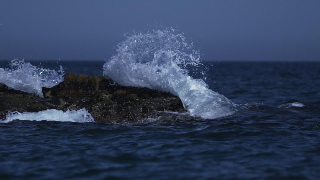 Small ocean waves crash against rocks in the Mediterranean Sea, 4K slow motion