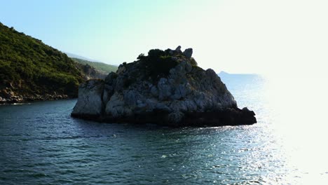 aerial-view-of-small-rocky-island-and-land-in-background-in-sunny-day