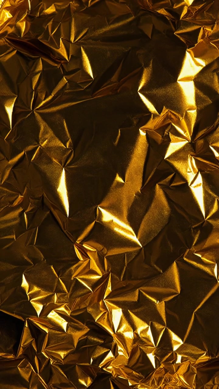 Una luce brillante scintilla su una superficie di foglia d'oro stropicciata in uno scatto ravvicinato di sfondo