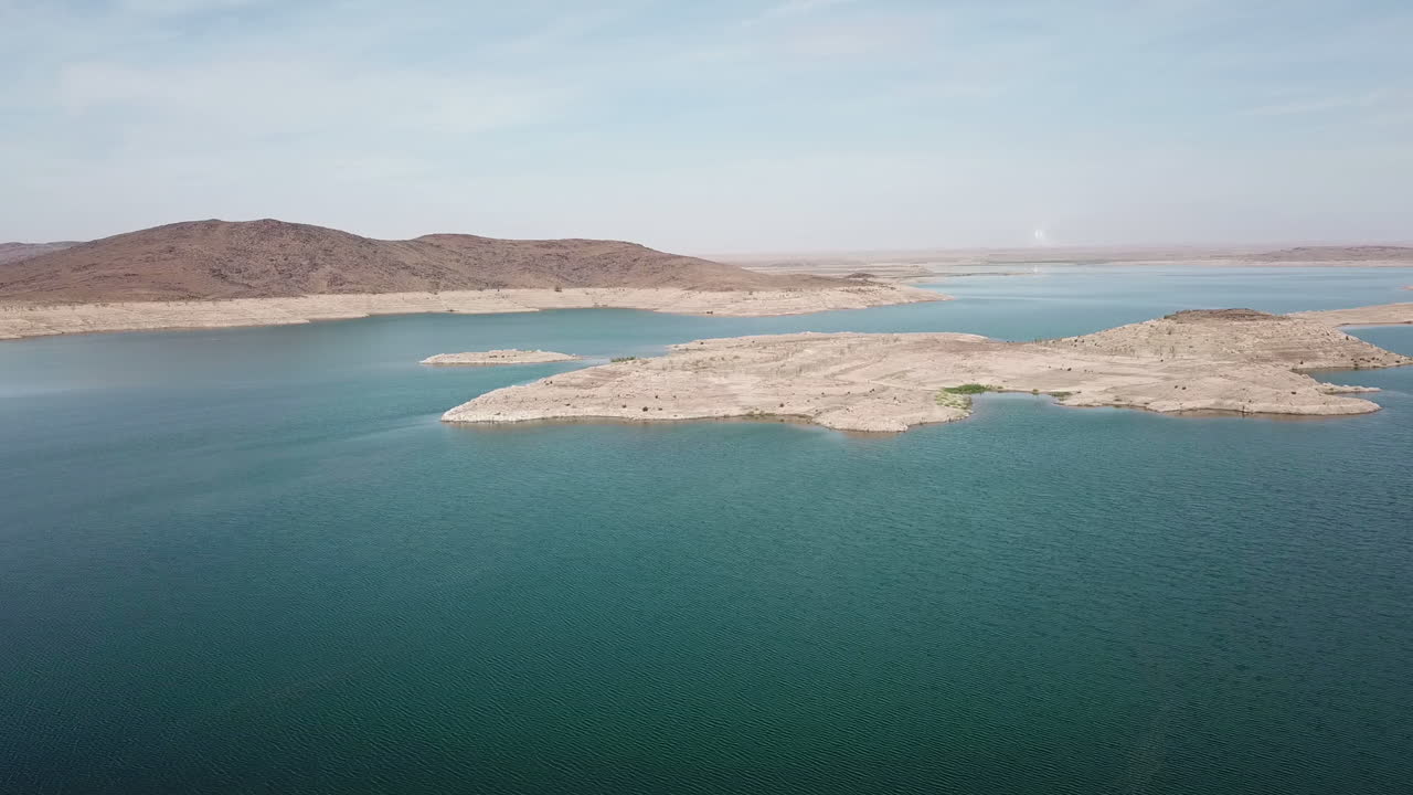 Ripresa aerea cinematografica 4K di un vasto bacino idrico turchese in un paesaggio arido e aspro. Contrasto mozzafiato tra acqua blu intenso e colline desertiche. Ideale per contenuti ambientali, sulle risorse idriche e di viaggio.