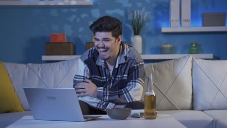 un joven viendo una película y bebiendo alcohol riéndose.