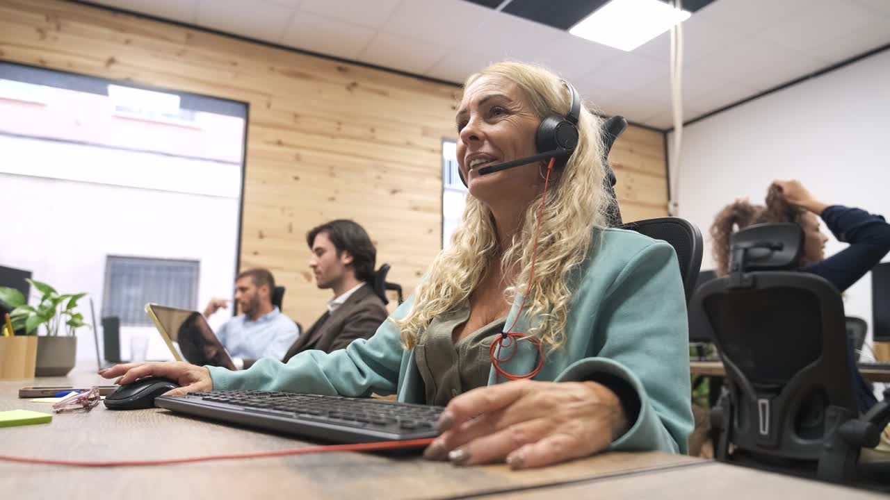 Happy mature businesswoman talking as she wears headset in coworking office