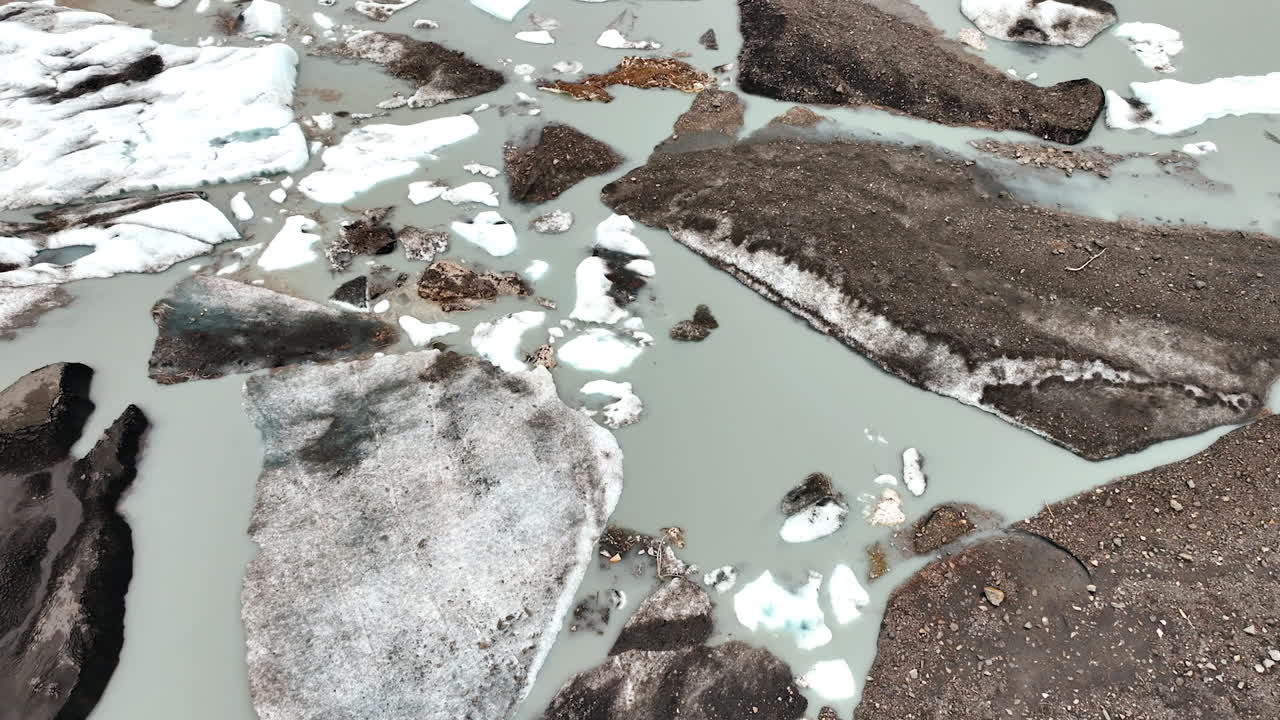 Flight over the grey waterscape with large boulders of melting ice. River or lake in Alaska from drone footage